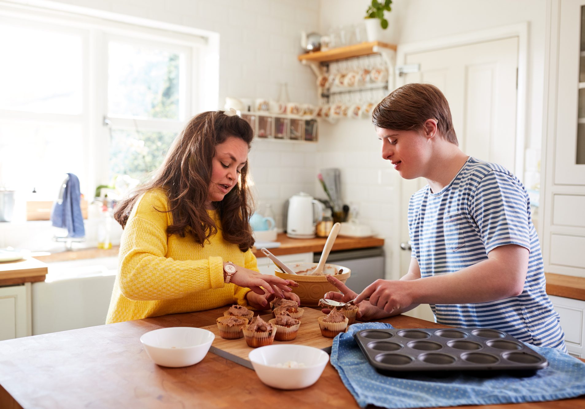 Young Downs Syndrome Couple Decorating Homemade Cupcakes With Icing In Kitchen At Home