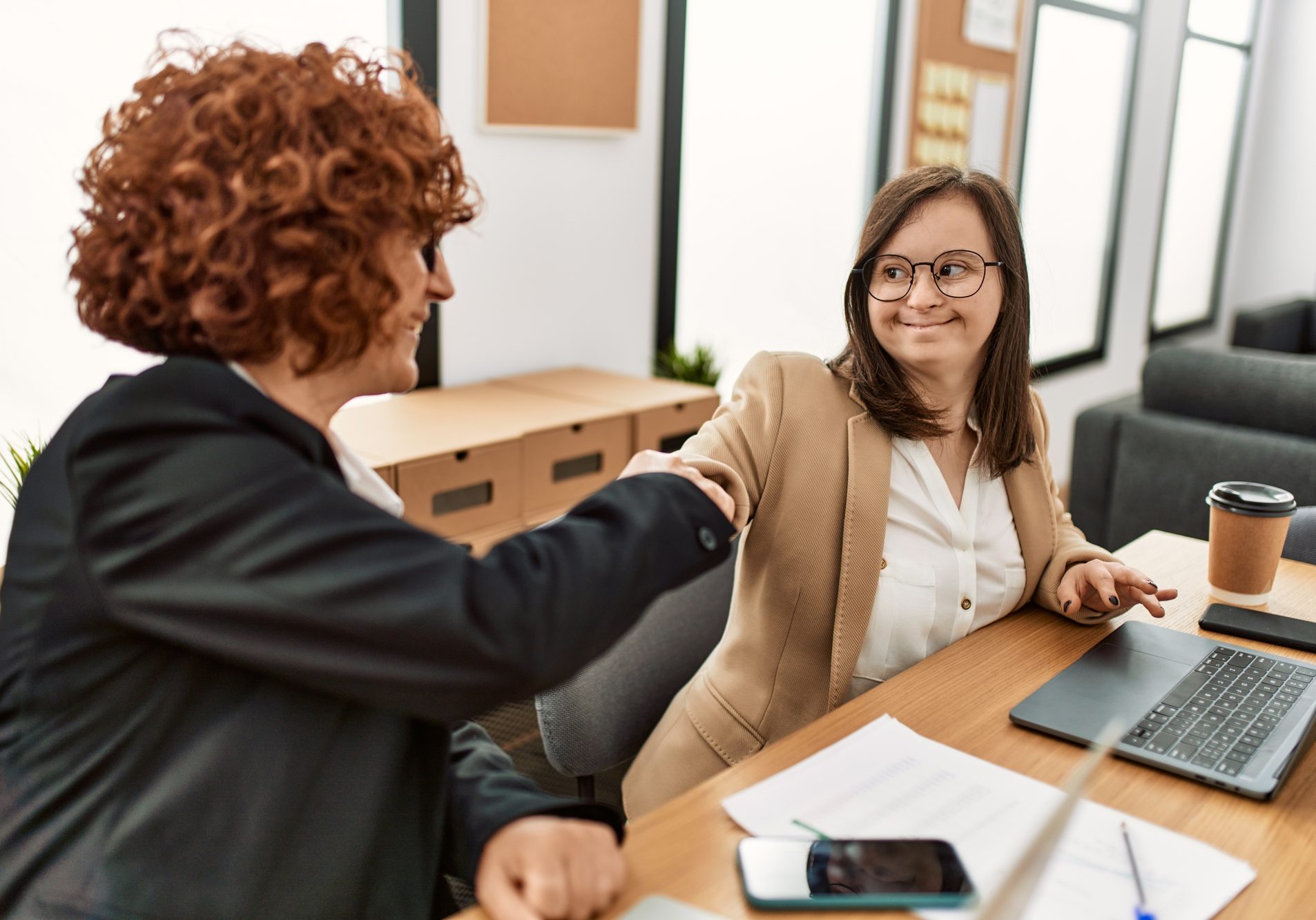 Group of two women working at the office. Mature woman and down syndrome girl working at inclusive teamwork.