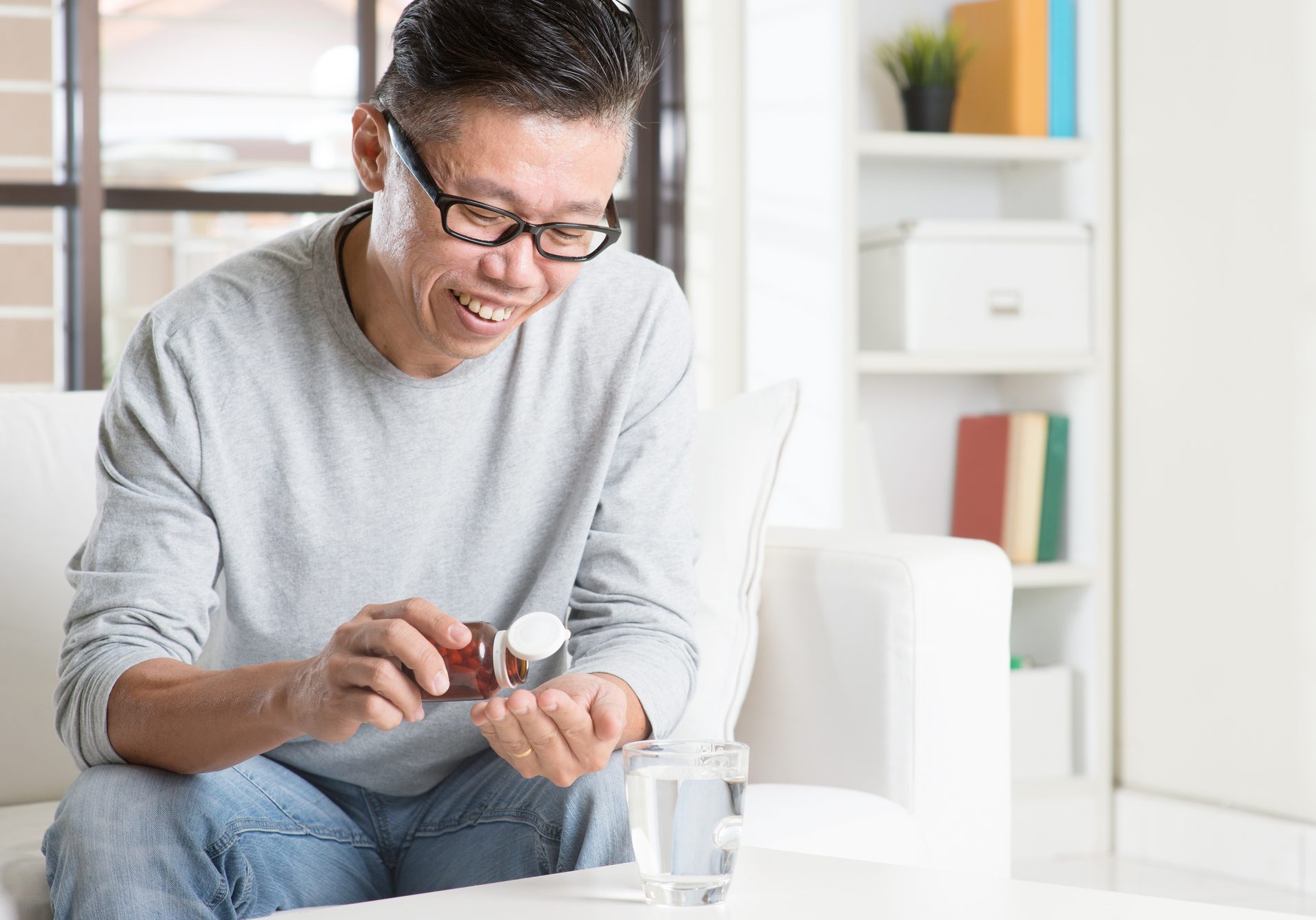 Men health concept. Portrait of 50s mature Asian man eating supplement, sitting on sofa at home.